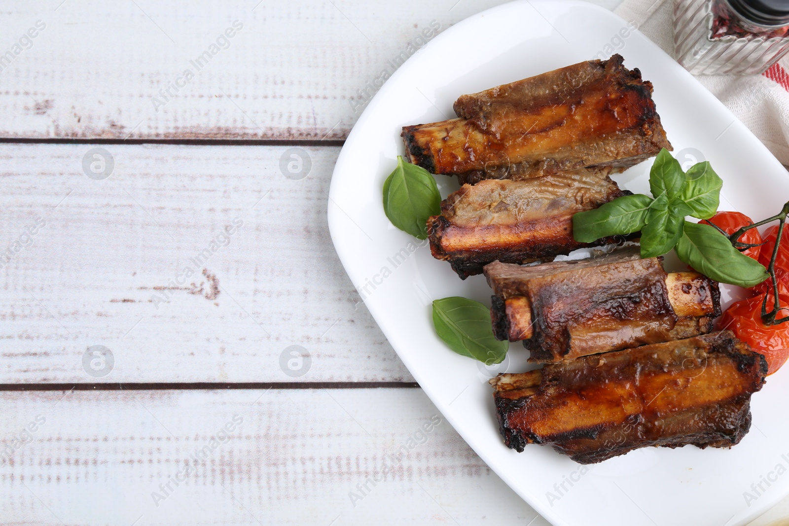 Roasted beef ribs, tomatoes and basil on white wooden table, top view. Space for text Photo of Roasted beef ribs, tomatoes and basil on white wooden table, top view. Space for text