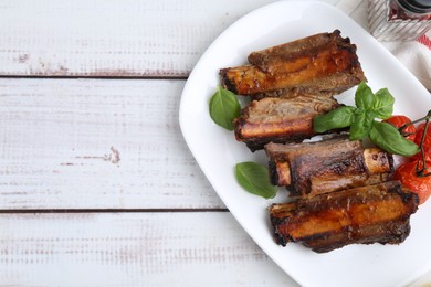 Photo of Roasted beef ribs, tomatoes and basil on white wooden table, top view. Space for text