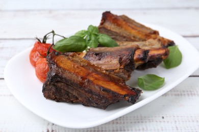 Photo of Roasted beef ribs, tomatoes and basil on white wooden table, closeup