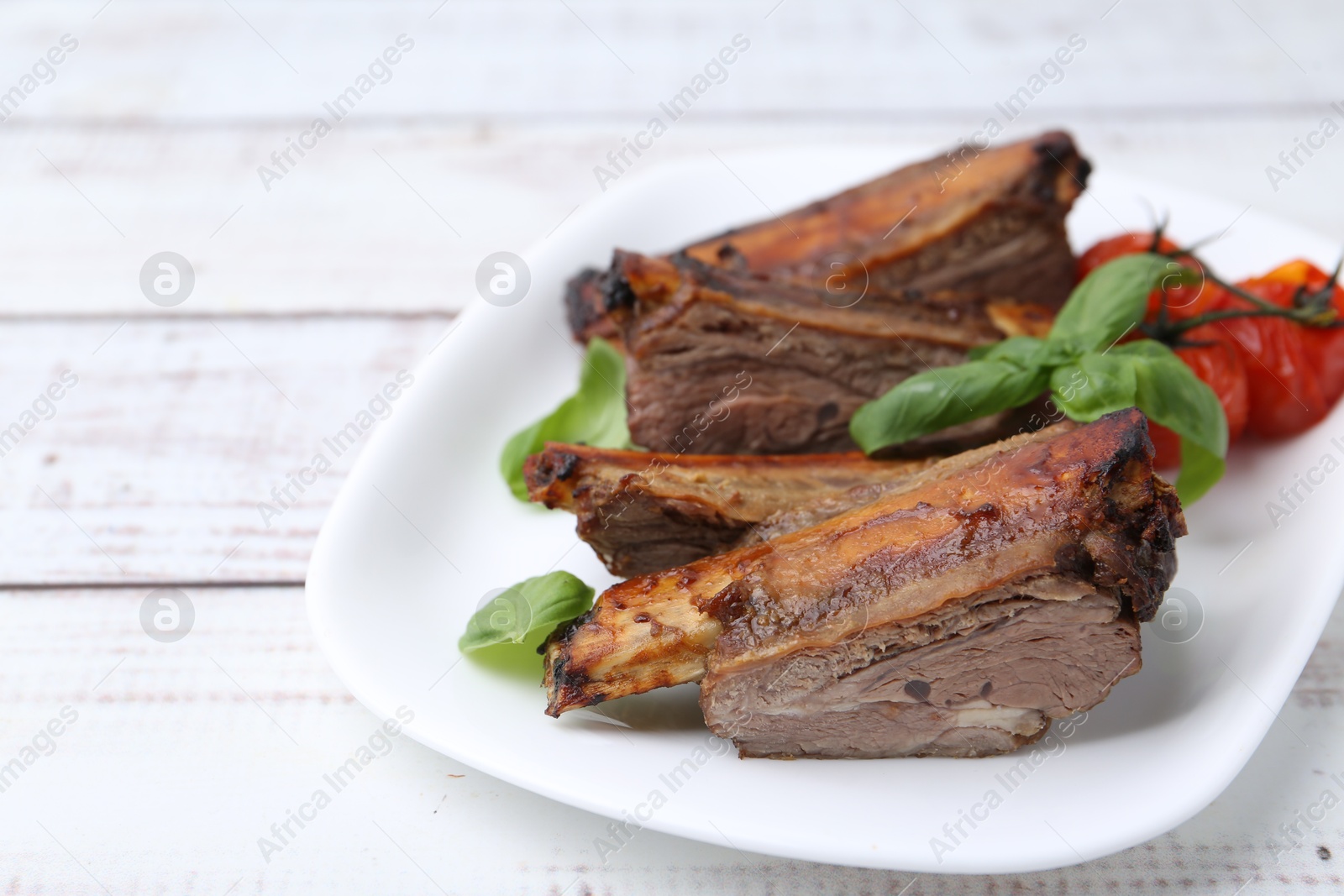 Roasted beef ribs, tomatoes and basil on white wooden table, closeup Photo of Roasted beef ribs, tomatoes and basil on white wooden table, closeup