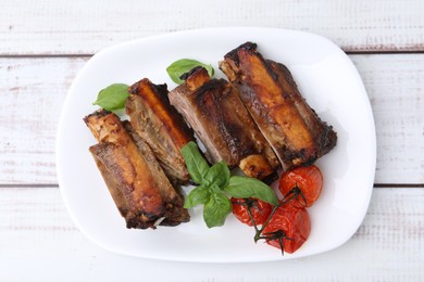 Photo of Roasted beef ribs, tomatoes and basil on white wooden table, top view
