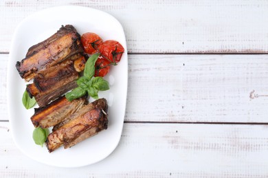 Photo of Roasted beef ribs, tomatoes and basil on white wooden table, top view. Space for text