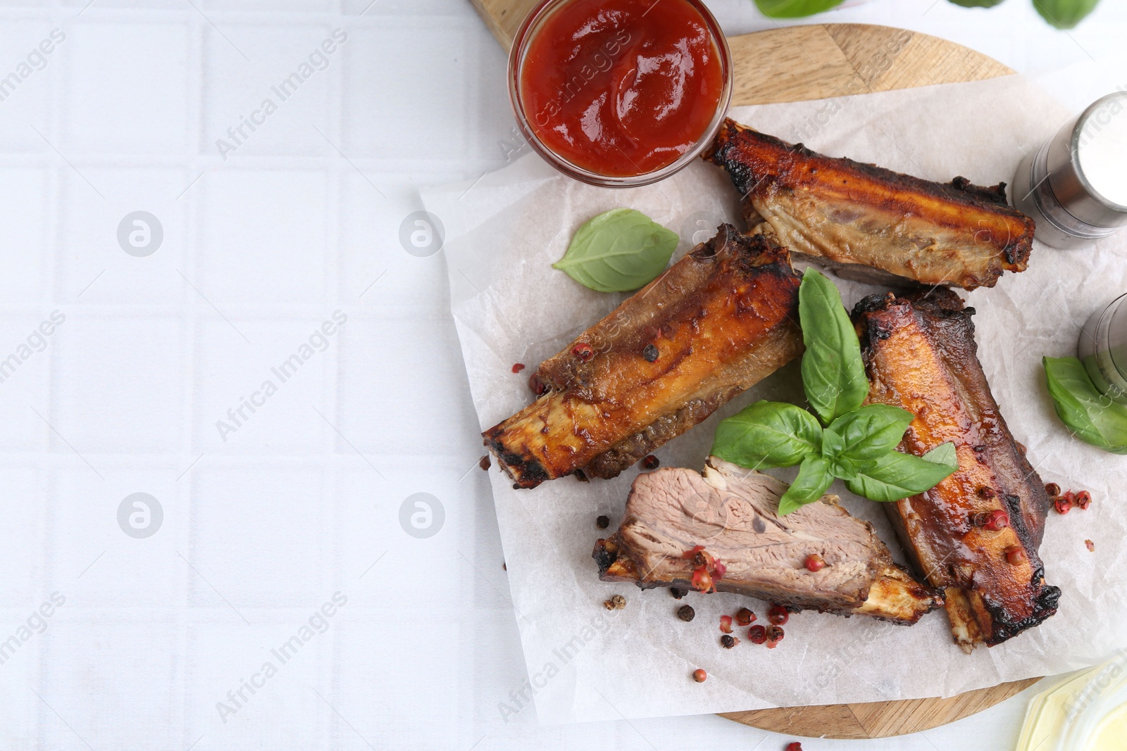 Roasted beef ribs with spices and ketchup on white tiled table, top view. Space for text Photo of Roasted beef ribs with spices and ketchup on white tiled table, top view. Space for text