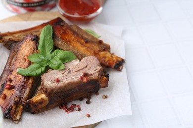 Photo of Roasted beef ribs with spices and ketchup on white tiled table, closeup. Space for text