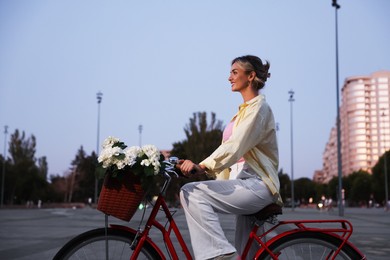 Photo of Beautiful woman riding bicycle with basket of flowers on city street