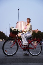 Photo of Beautiful woman riding bicycle with basket of flowers on city street