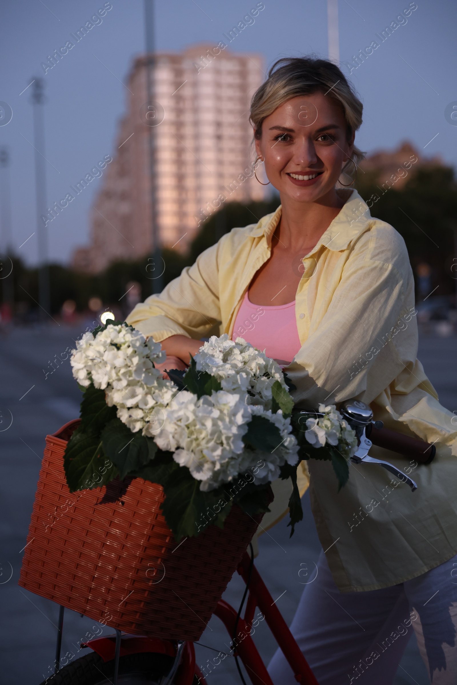 Beautiful woman near bicycle with basket of flowers on city street Photo of Beautiful woman near bicycle with basket of flowers on city street