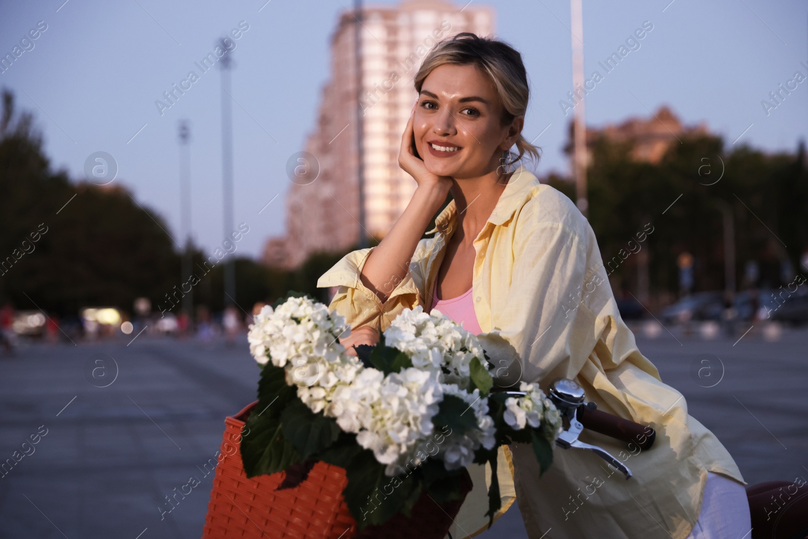 Photo of Beautiful woman near bicycle with basket of flowers on city street, space for text