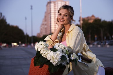 Photo of Beautiful woman near bicycle with basket of flowers on city street, space for text