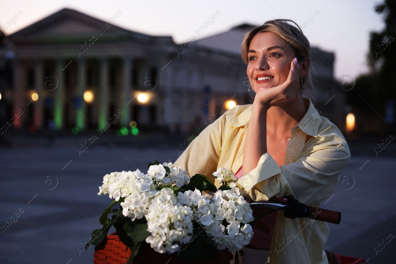 Photo of Beautiful woman near bicycle with basket of flowers on city street, space for text