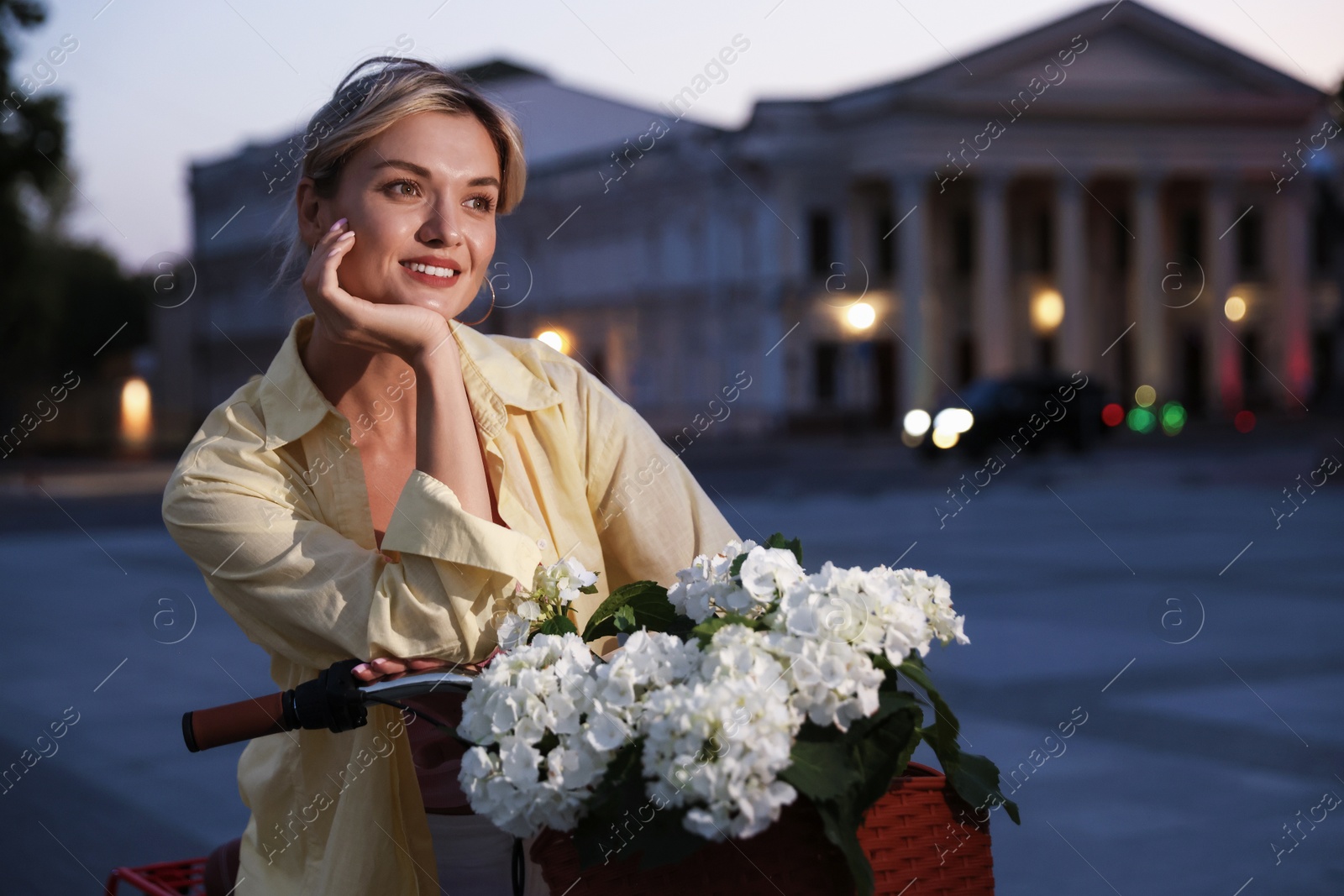 Photo of Beautiful woman near bicycle with basket of flowers on city street, space for text