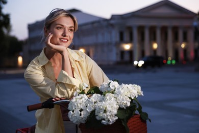 Photo of Beautiful woman near bicycle with basket of flowers on city street, space for text