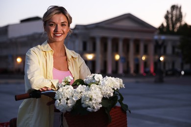 Photo of Beautiful woman near bicycle with basket of flowers on city street, space for text