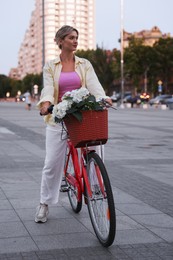 Photo of Beautiful woman riding bicycle with basket of flowers on city street