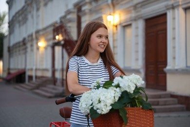 Photo of Beautiful teenage girl on bicycle with basket of flowers outdoors