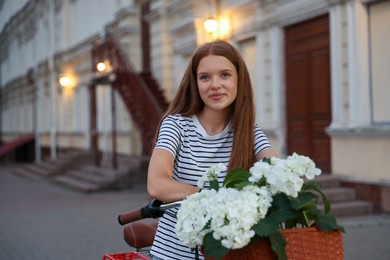 Photo of Beautiful teenage girl on bicycle with basket of flowers outdoors, space for text
