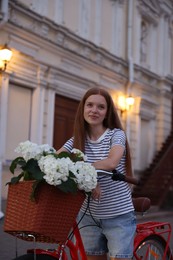 Photo of Beautiful teenage girl on bicycle with basket of flowers outdoors