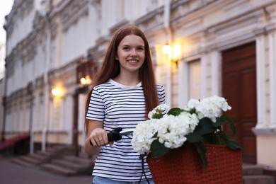 Photo of Beautiful teenage girl near bicycle with basket of flowers on city street