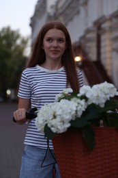 Photo of Beautiful teenage girl near bicycle with basket of flowers on city street
