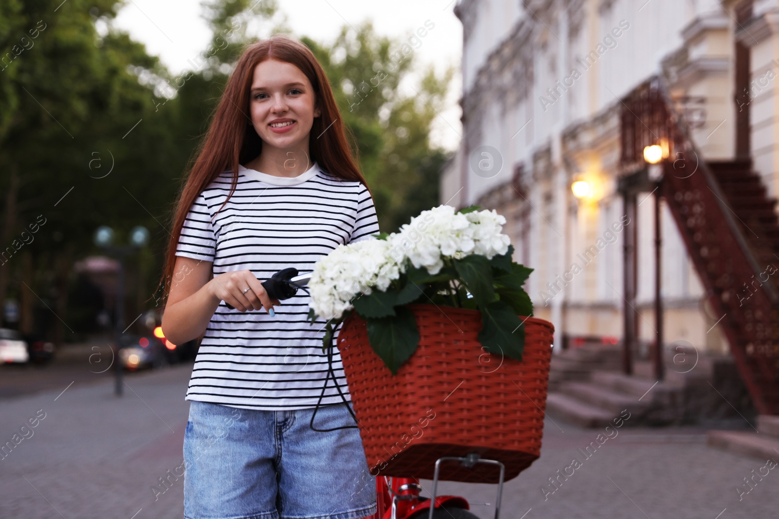 Photo of Beautiful teenage girl near bicycle with basket of flowers on city street