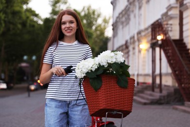 Photo of Beautiful teenage girl near bicycle with basket of flowers on city street