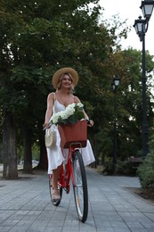 Photo of Beautiful woman riding bicycle with basket of flowers on city street