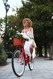 Photo of Beautiful woman riding bicycle with basket of flowers on city street, low angle view