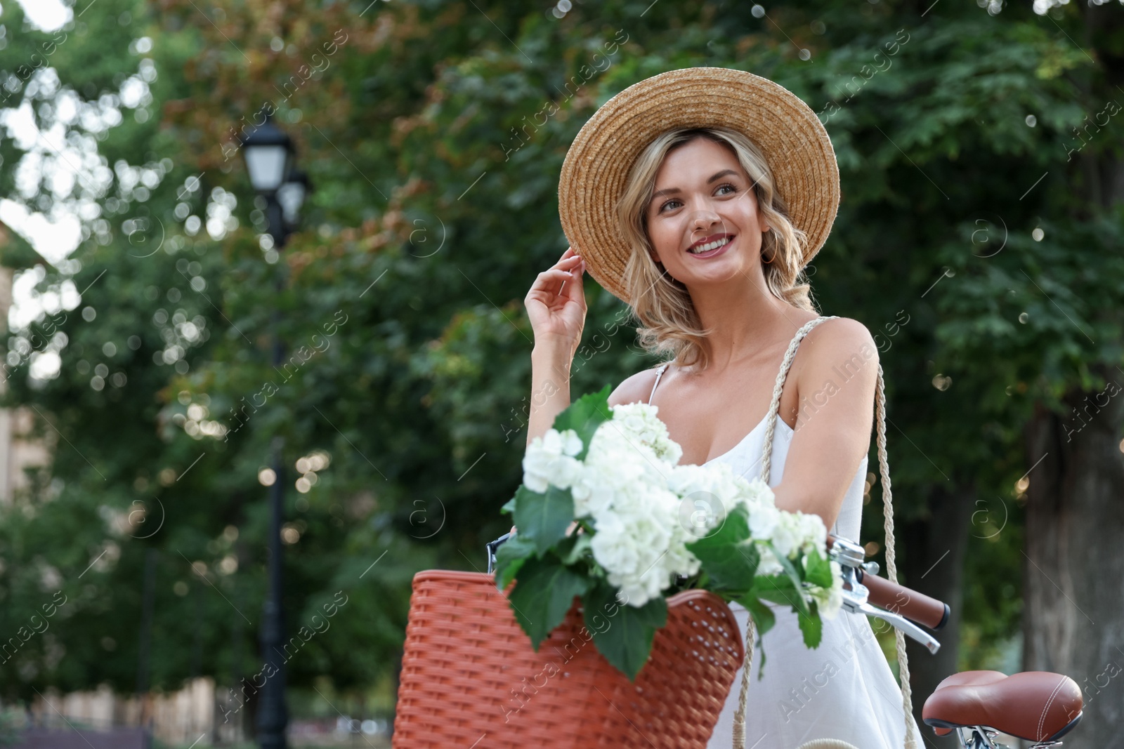 Beautiful woman near bicycle with basket of flowers on city street, space for text Photo of Beautiful woman near bicycle with basket of flowers on city street, space for text