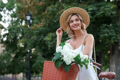 Photo of Beautiful woman near bicycle with basket of flowers on city street, space for text