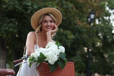 Photo of Beautiful woman near bicycle with basket of flowers on city street, space for text