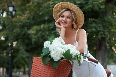 Photo of Beautiful woman near bicycle with basket of flowers on city street, space for text