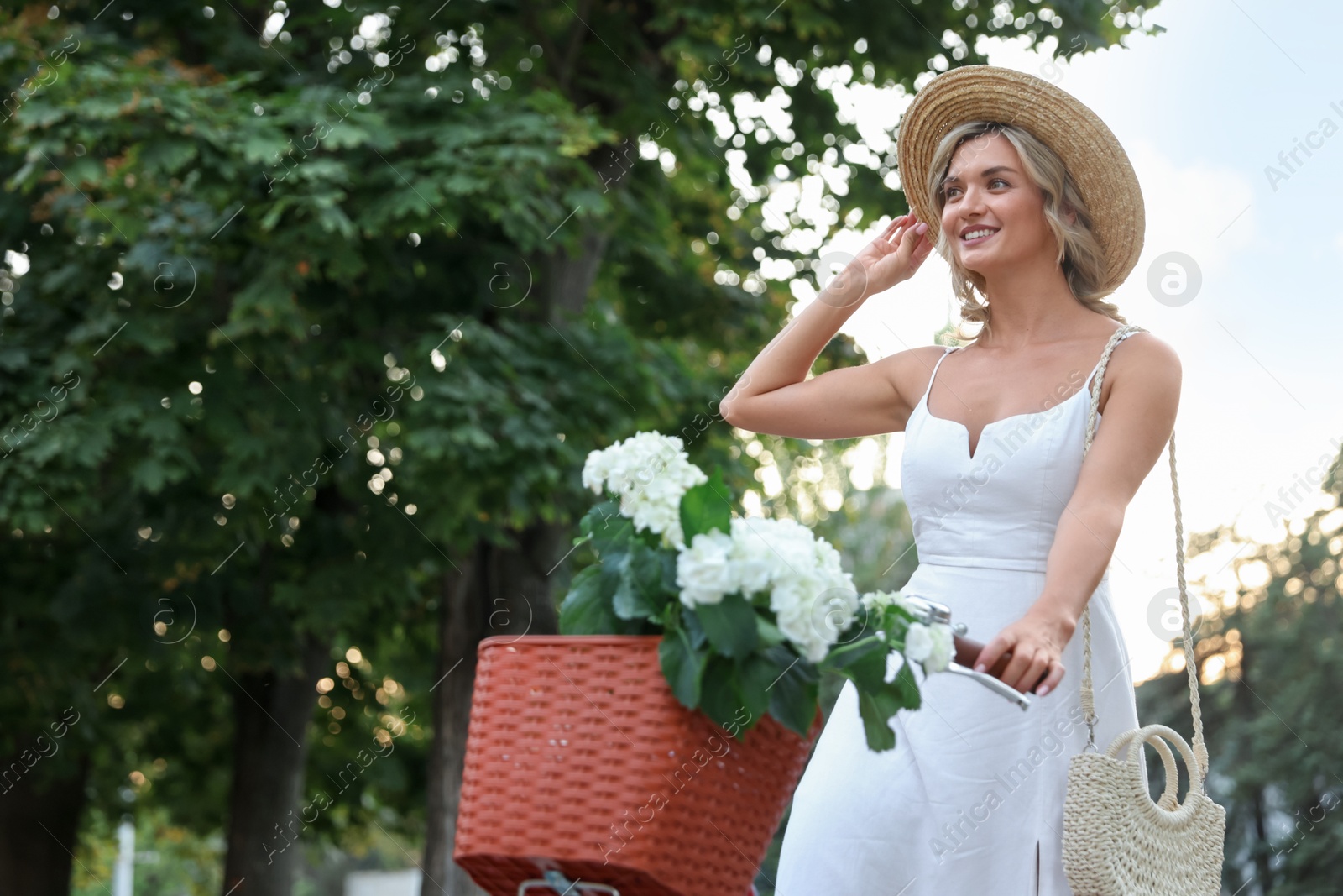 Photo of Beautiful woman on bicycle with basket of flowers outdoors, space for text