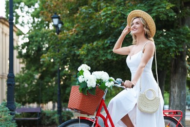 Photo of Beautiful woman riding bicycle with basket of flowers on city street
