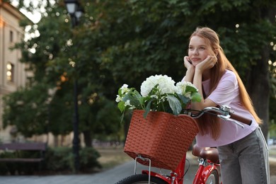 Photo of Beautiful teenage girl near bicycle with basket of flowers on city street, space for text