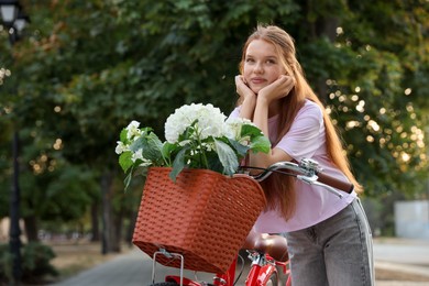 Photo of Beautiful teenage girl near bicycle with basket of flowers on city street