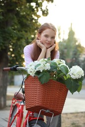 Photo of Beautiful teenage girl near bicycle with basket of flowers on city street
