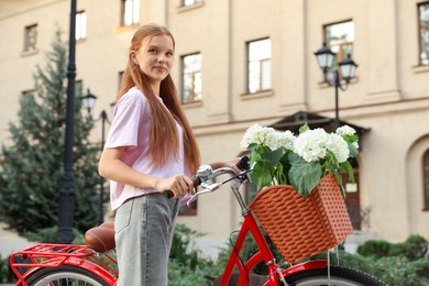 Photo of Beautiful teenage girl near bicycle with basket of flowers on city street, low angle view