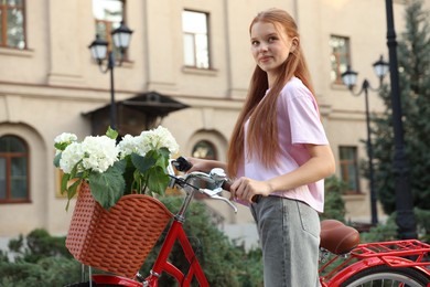Photo of Beautiful teenage girl near bicycle with basket of flowers on city street, low angle view