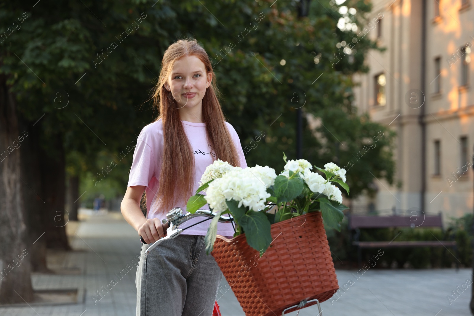 Photo of Beautiful teenage girl near bicycle with basket of flowers on city street
