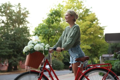 Photo of Beautiful woman near bicycle with basket of flowers on city street