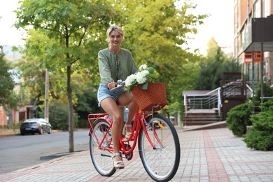 Photo of Beautiful woman riding bicycle with basket of flowers on city street