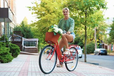 Photo of Beautiful woman riding bicycle with basket of flowers on city street