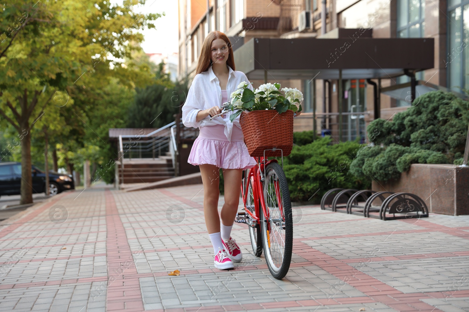 Beautiful teenage girl near bicycle with basket of flowers on city street Photo of Beautiful teenage girl near bicycle with basket of flowers on city street