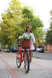 Photo of Beautiful teenage girl near bicycle with basket of flowers on city street
