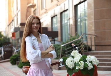 Photo of Beautiful teenage girl near bicycle with basket of flowers on city street