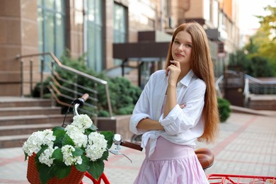 Photo of Beautiful teenage girl near bicycle with basket of flowers on city street