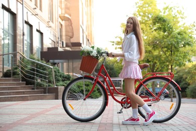 Photo of Beautiful teenage girl near bicycle with basket of flowers on city street