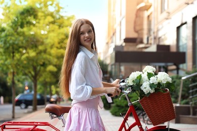 Photo of Beautiful teenage girl near bicycle with basket of flowers on city street