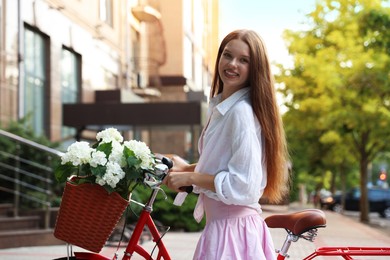 Photo of Beautiful teenage girl near bicycle with basket of flowers on city street