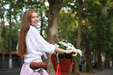 Photo of Beautiful teenage girl near bicycle with basket of flowers on city street